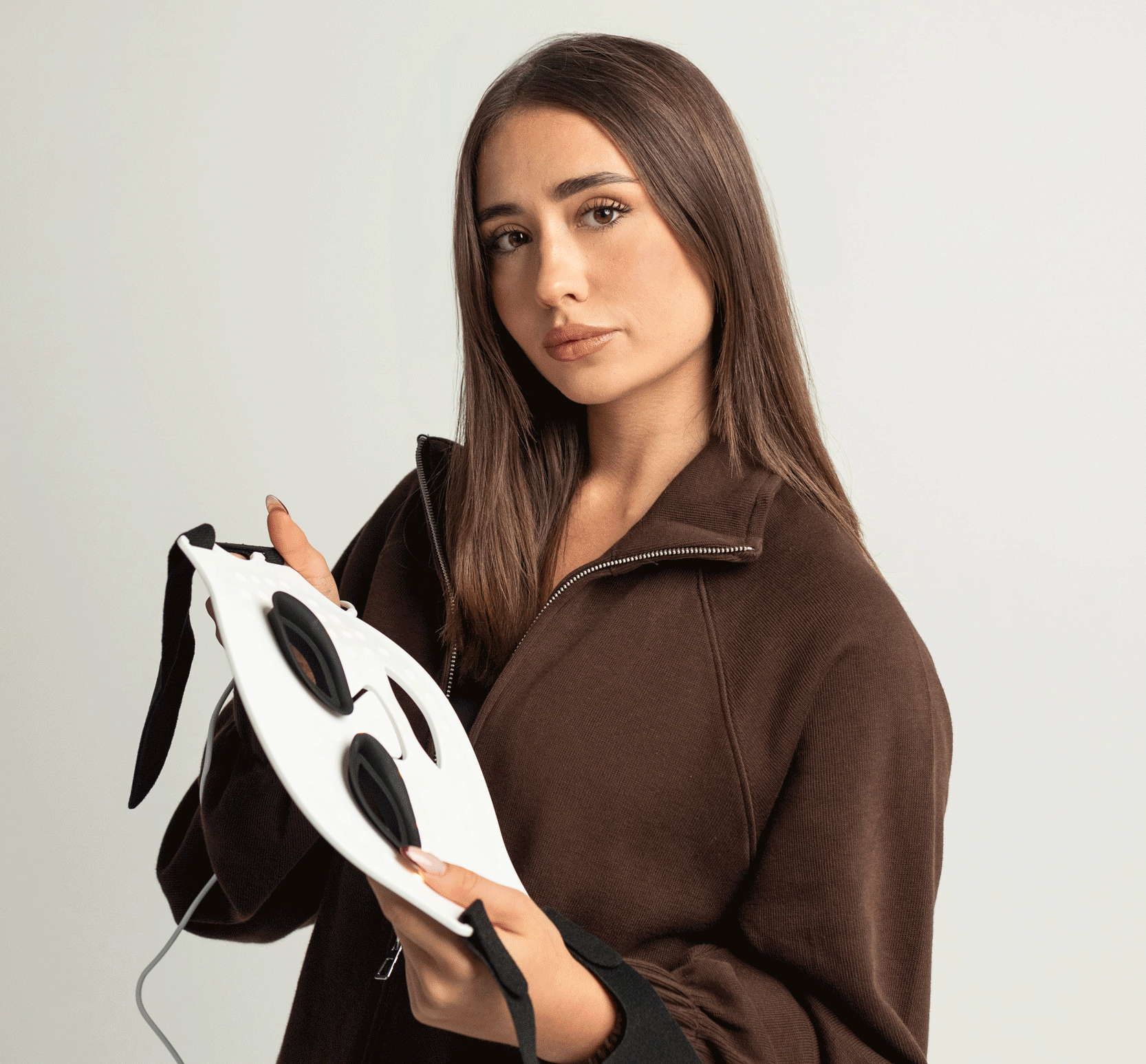 Žena drží LumenLuxe LED masku na tvár — pohľad zboku na dizajn a nastaviteľné popruhy